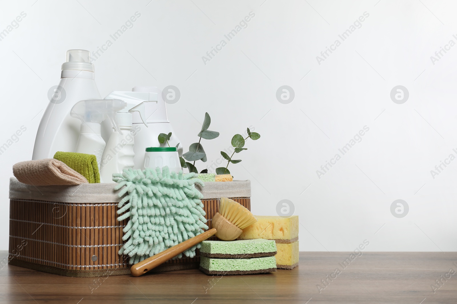 Photo of Eco-friendly cleaning products, supplies and eucalyptus branches in basket on wooden table, space for text