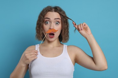 Photo of Surprised woman with fake paper mustache on light blue background