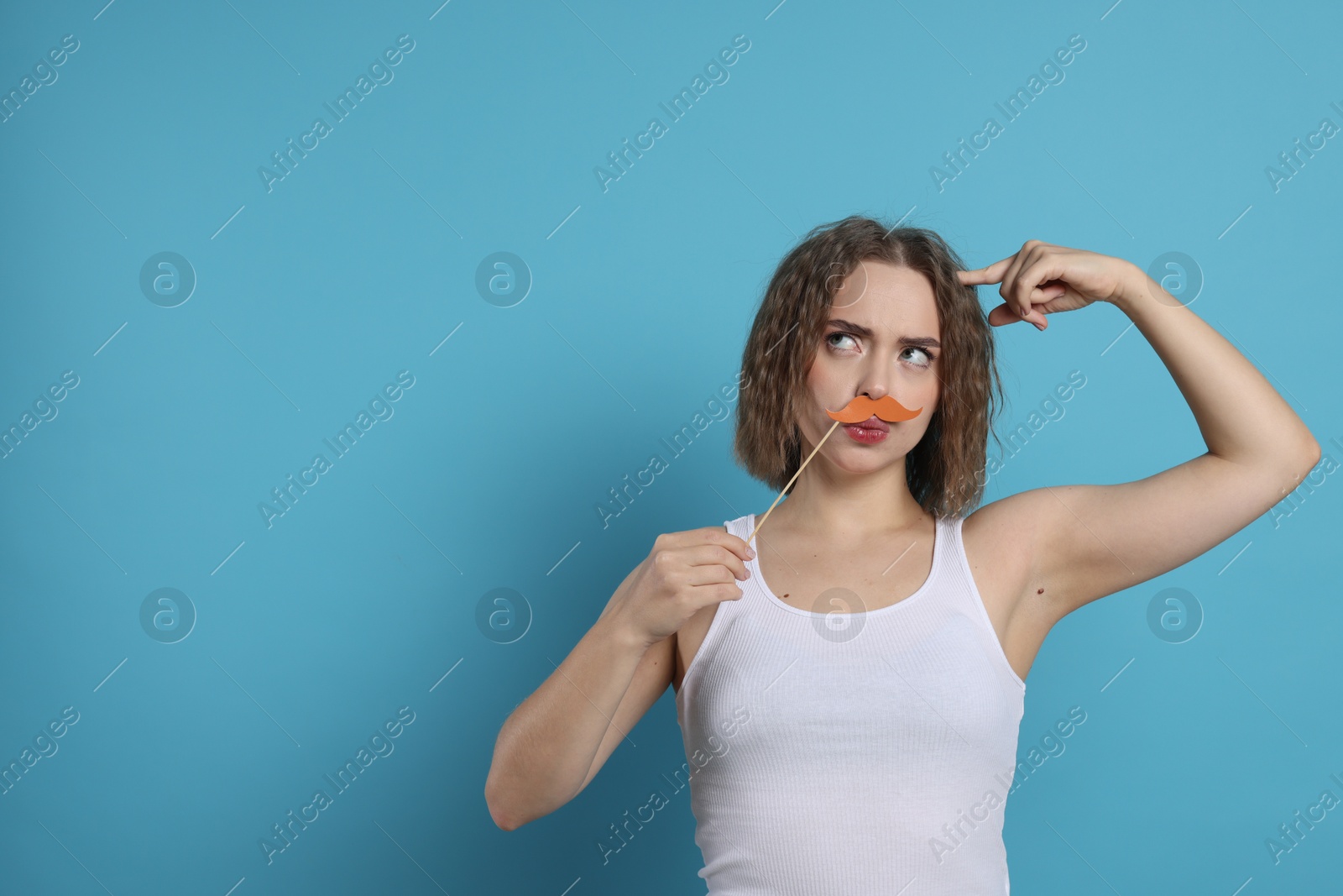 Photo of Thoughtful woman with fake paper mustache on light blue background. Space for text