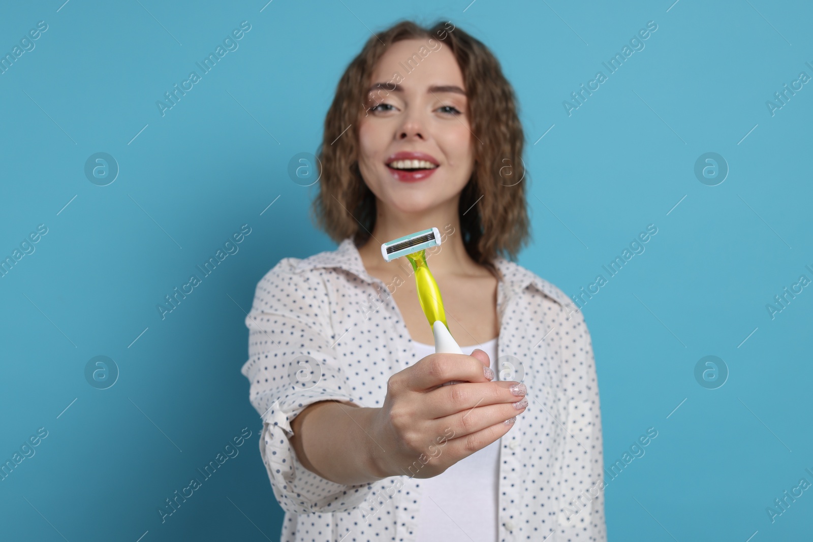 Photo of Happy woman giving razor on light blue background, selective focus. Hair removal tool