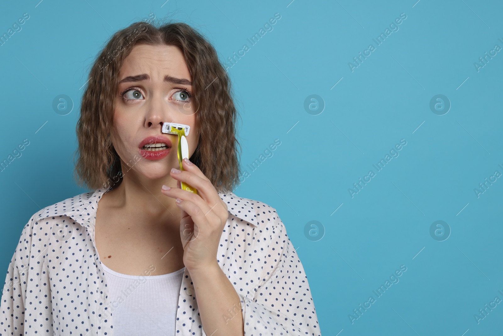 Photo of Emotional woman shaving her mustache with razor on light blue background. Space for text