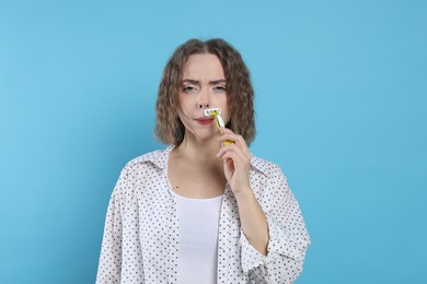 Photo of Woman shaving her mustache with razor on light blue background