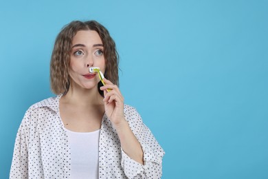 Photo of Woman shaving her mustache with razor on light blue background. Space for text