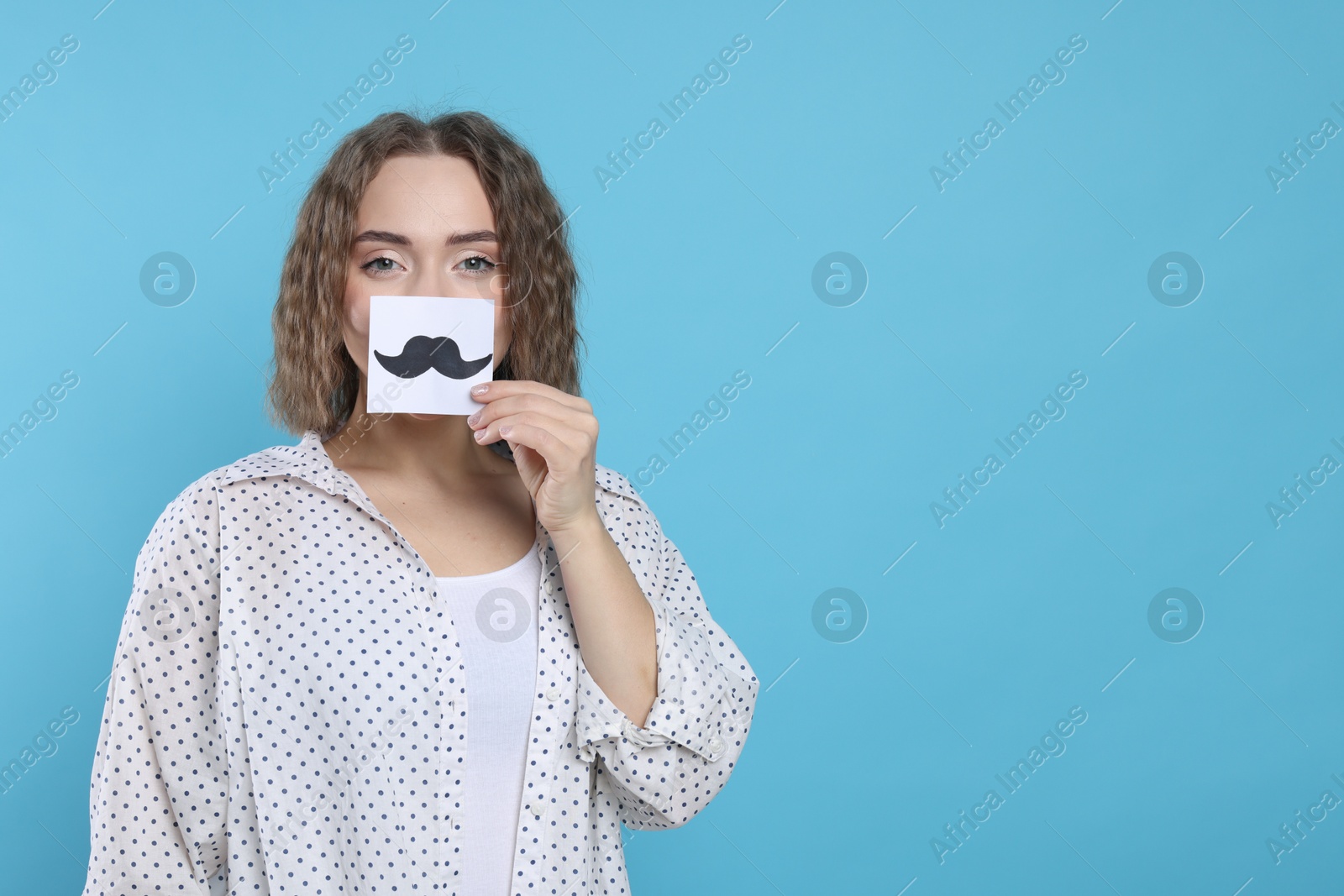 Photo of Woman holding paper with drawn mustache on light blue background, space for text