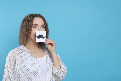 Photo of Woman holding paper with drawn mustache on light blue background, space for text