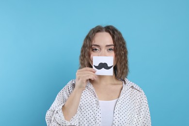 Photo of Woman holding paper with drawn mustache on light blue background