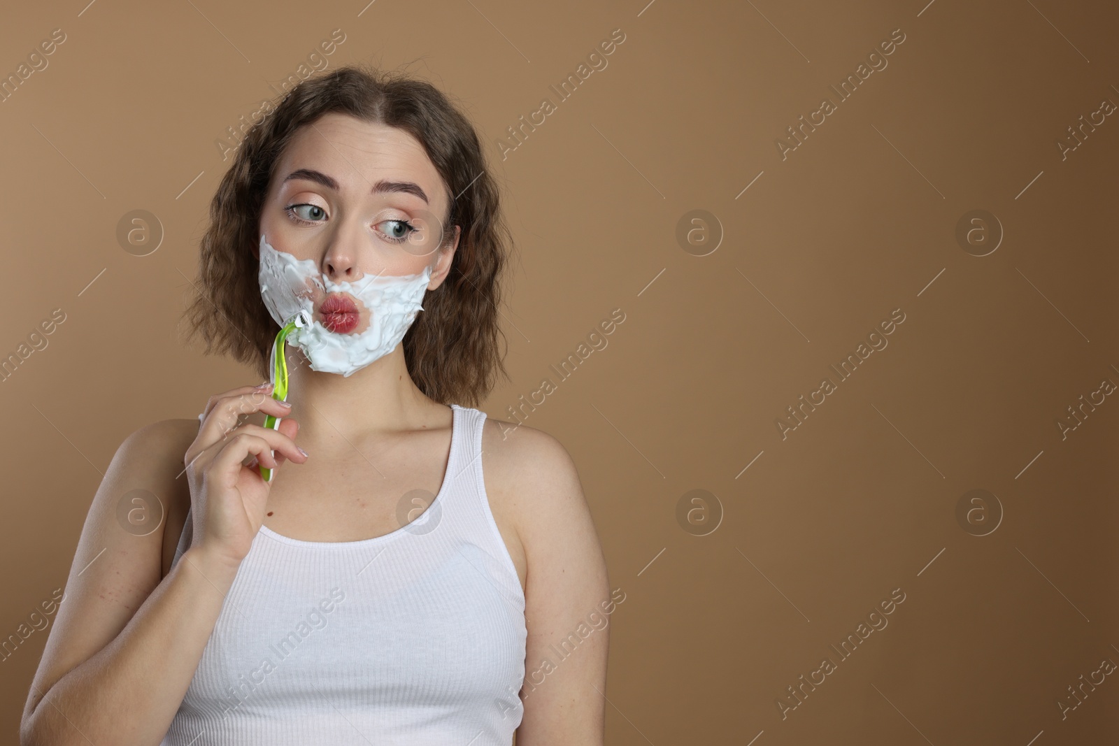 Photo of Funny woman shaving facial hair with razor on beige background. Space for text