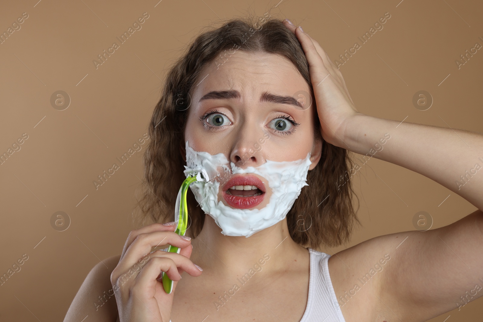 Photo of Emotional woman shaving facial hair with razor on beige background