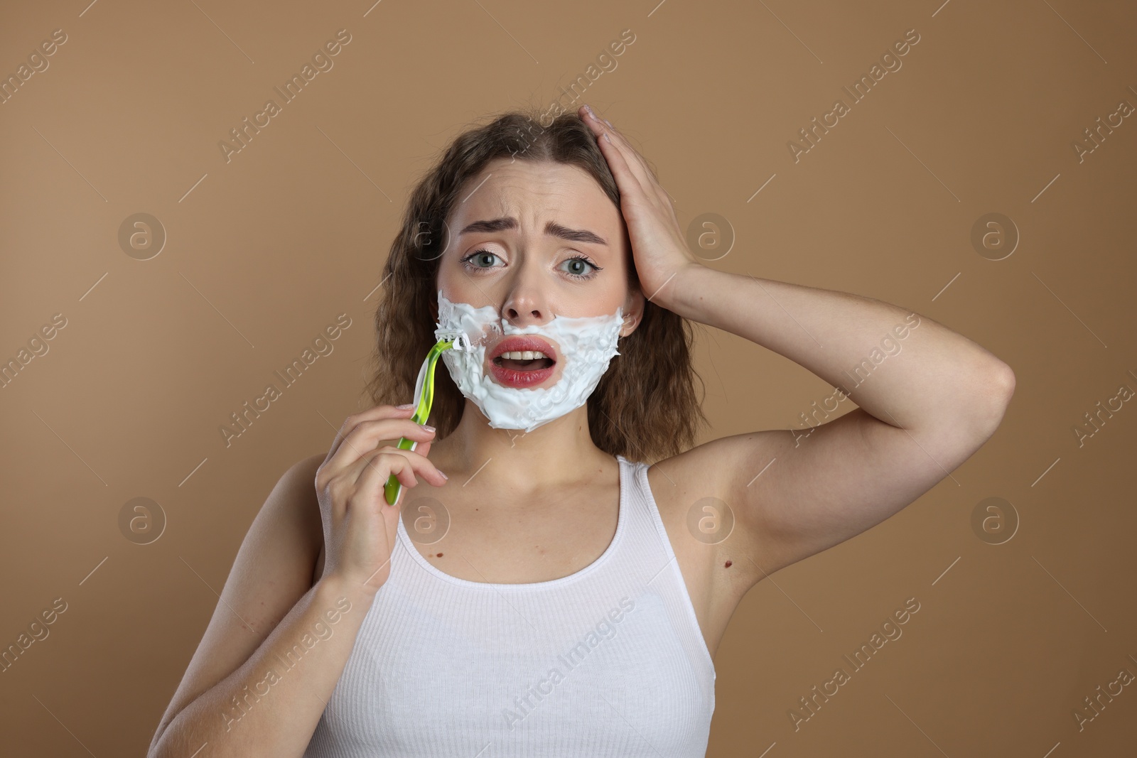 Photo of Emotional woman shaving facial hair with razor on beige background