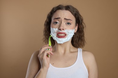 Photo of Emotional woman shaving facial hair with razor on beige background