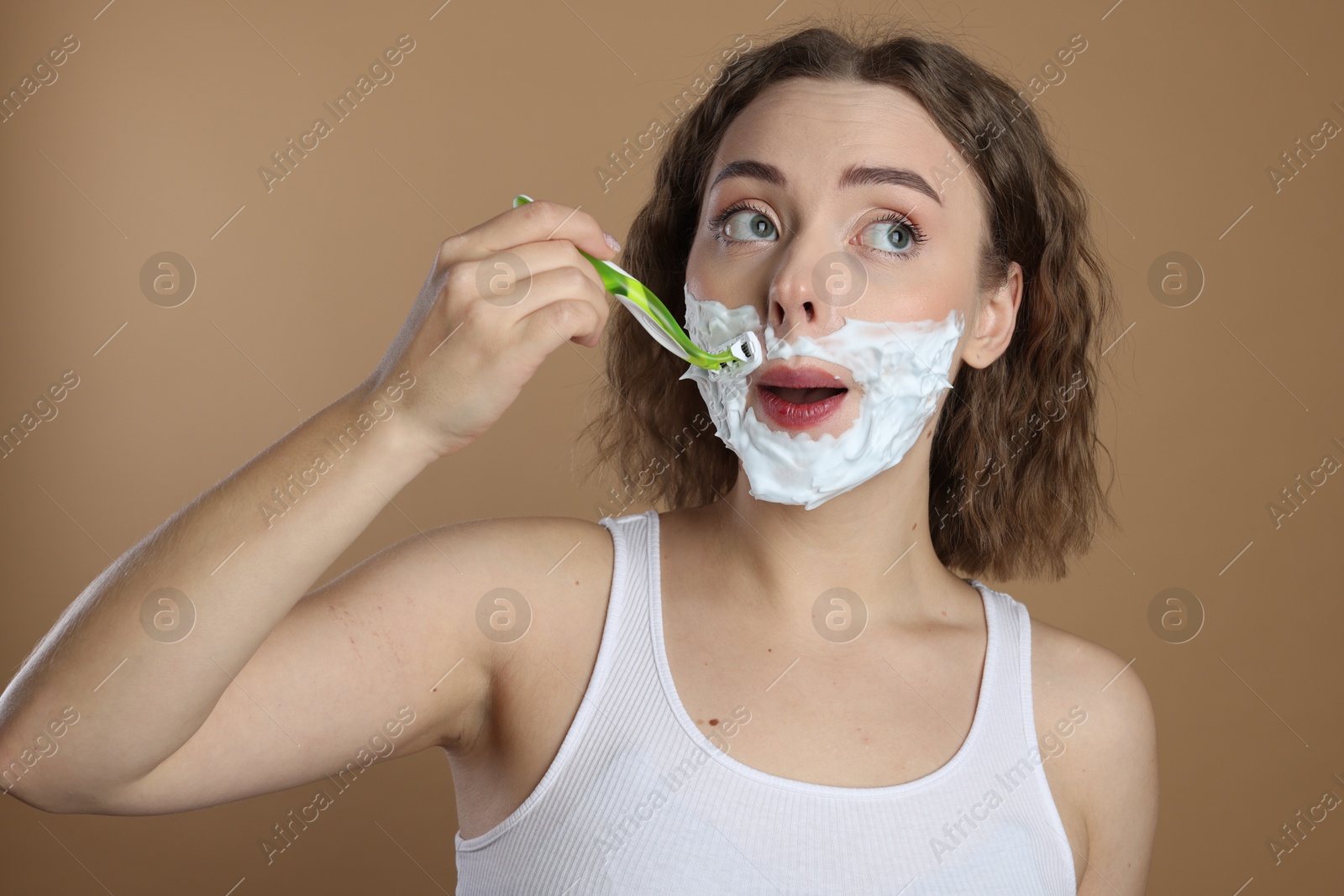 Photo of Funny woman shaving mustache with razor on beige background