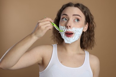 Photo of Funny woman shaving mustache with razor on beige background