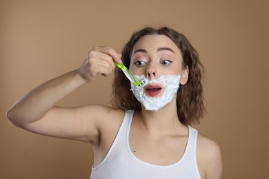 Photo of Funny woman shaving mustache with razor on beige background