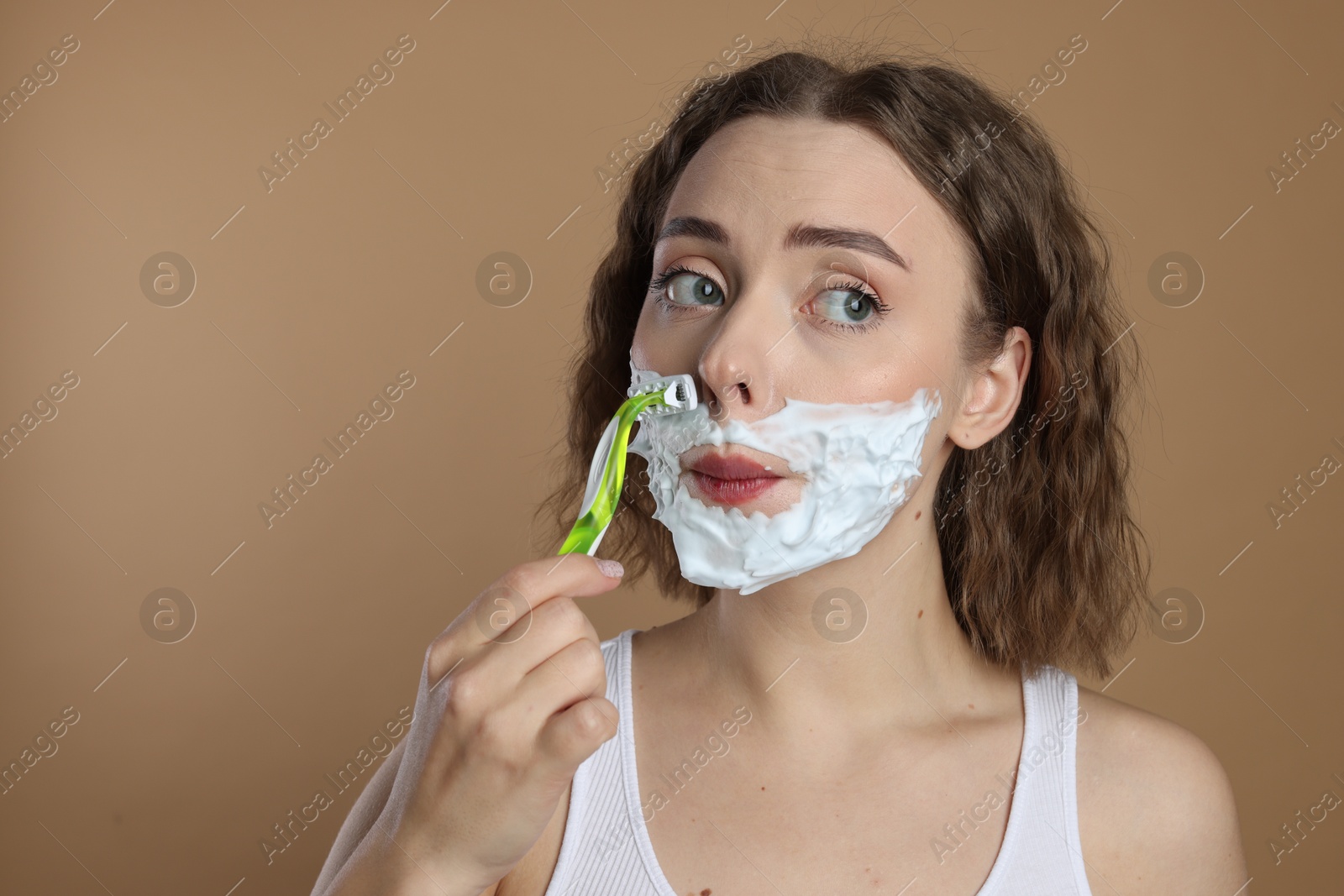 Photo of Funny woman shaving facial hair with razor on beige background. Space for text