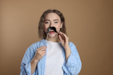 Photo of Happy woman with fake paper mustache on beige background