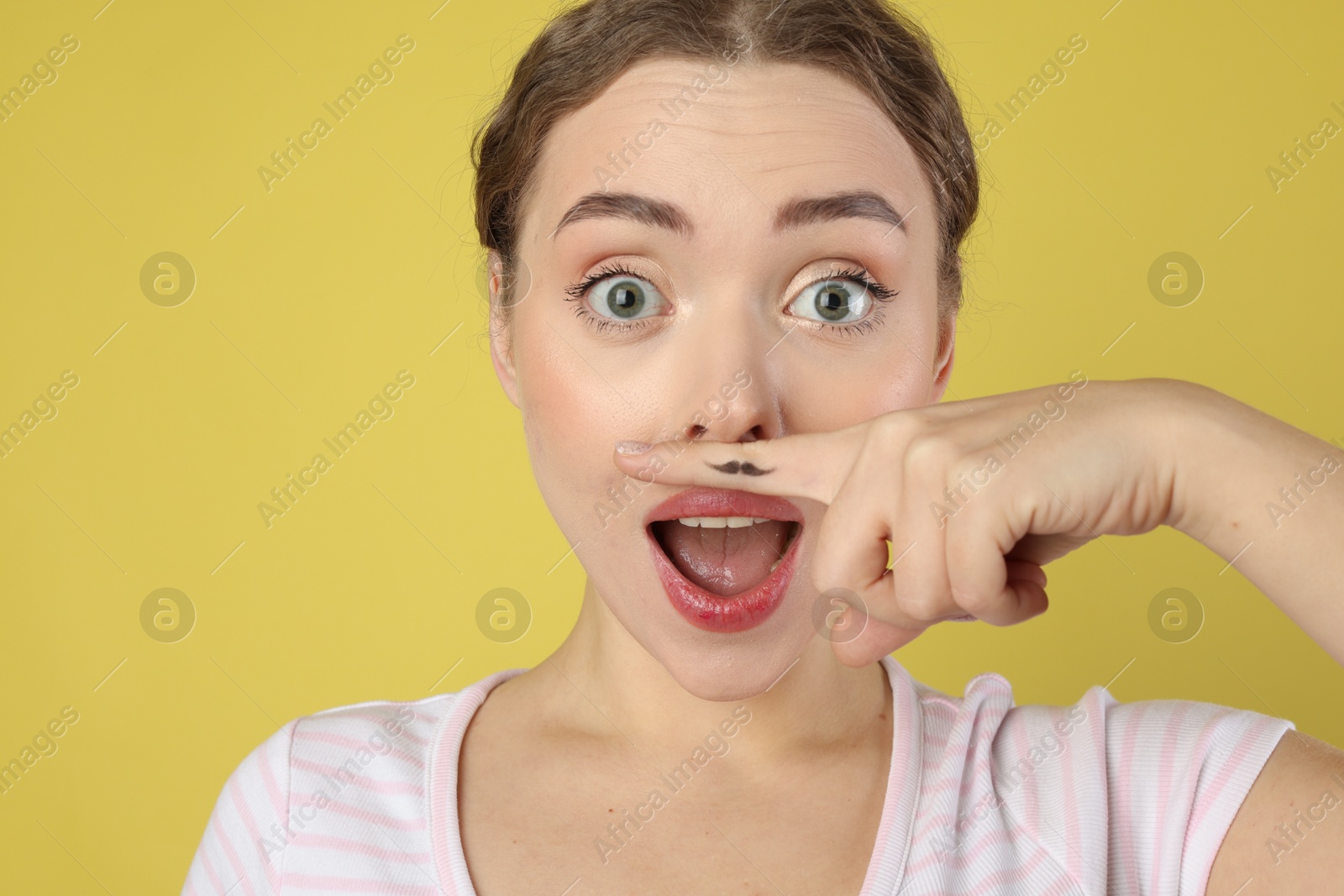 Photo of Emotional woman holding finger with drawn mustache above lips on light green background