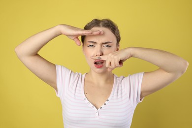 Photo of Funny woman holding finger with drawn mustache above lips on light green background