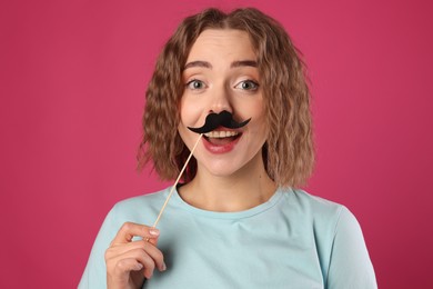 Photo of Happy woman with fake paper mustache on pink background