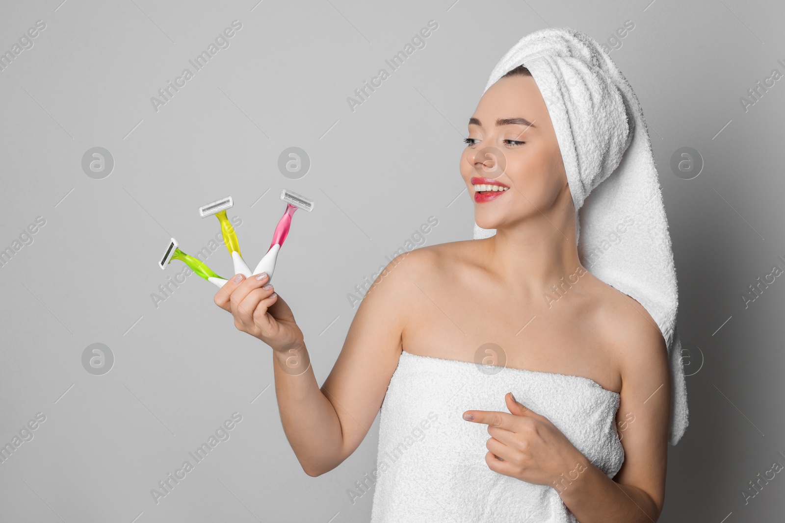 Photo of Happy woman pointing at different razors on grey background. Hair removal tools