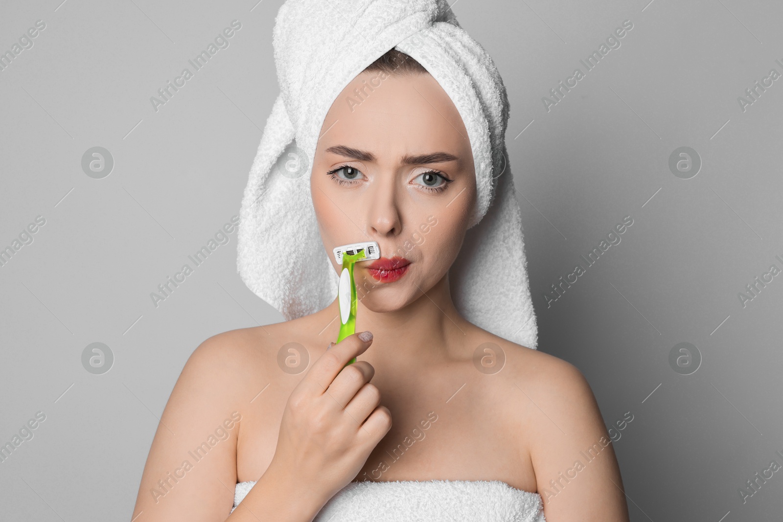 Photo of Beautiful woman shaving her mustache with razor on grey background