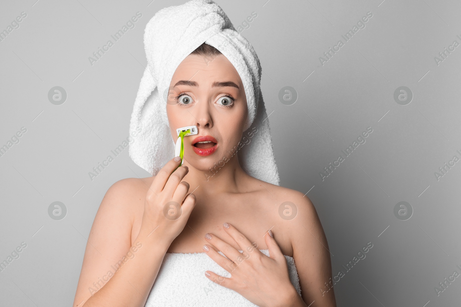 Photo of Emotional woman shaving her mustache with razor on grey background