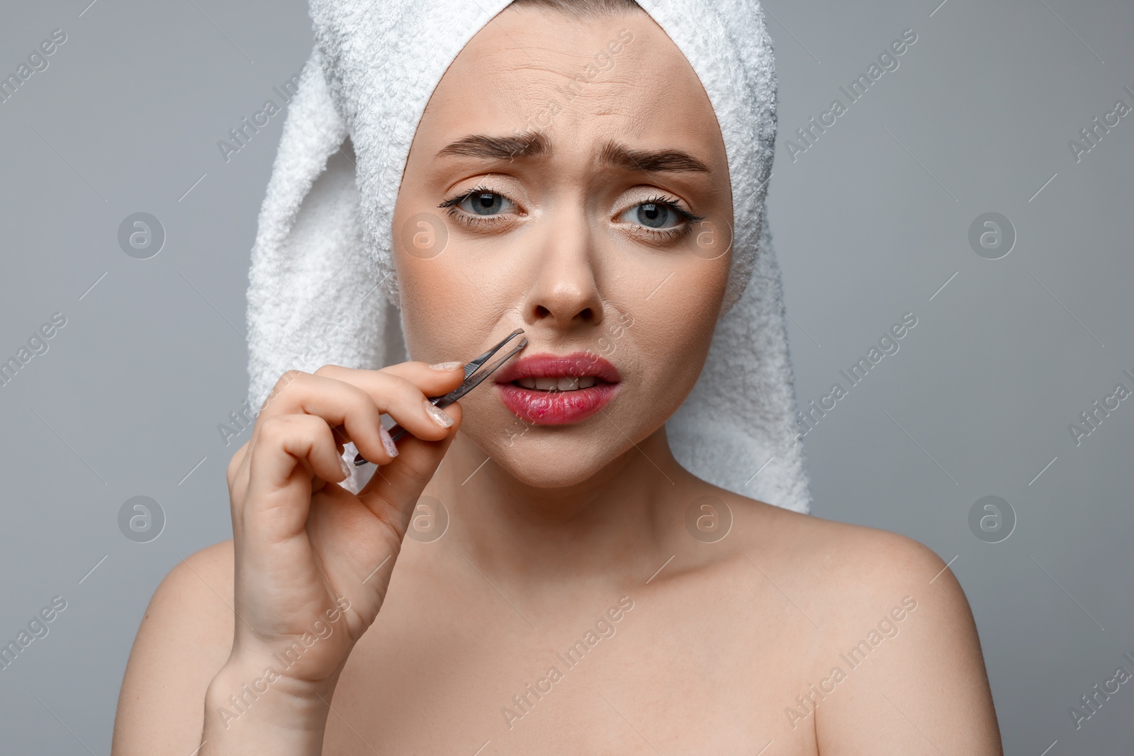 Photo of Beautiful woman plucking her mustache with tweezers on grey background