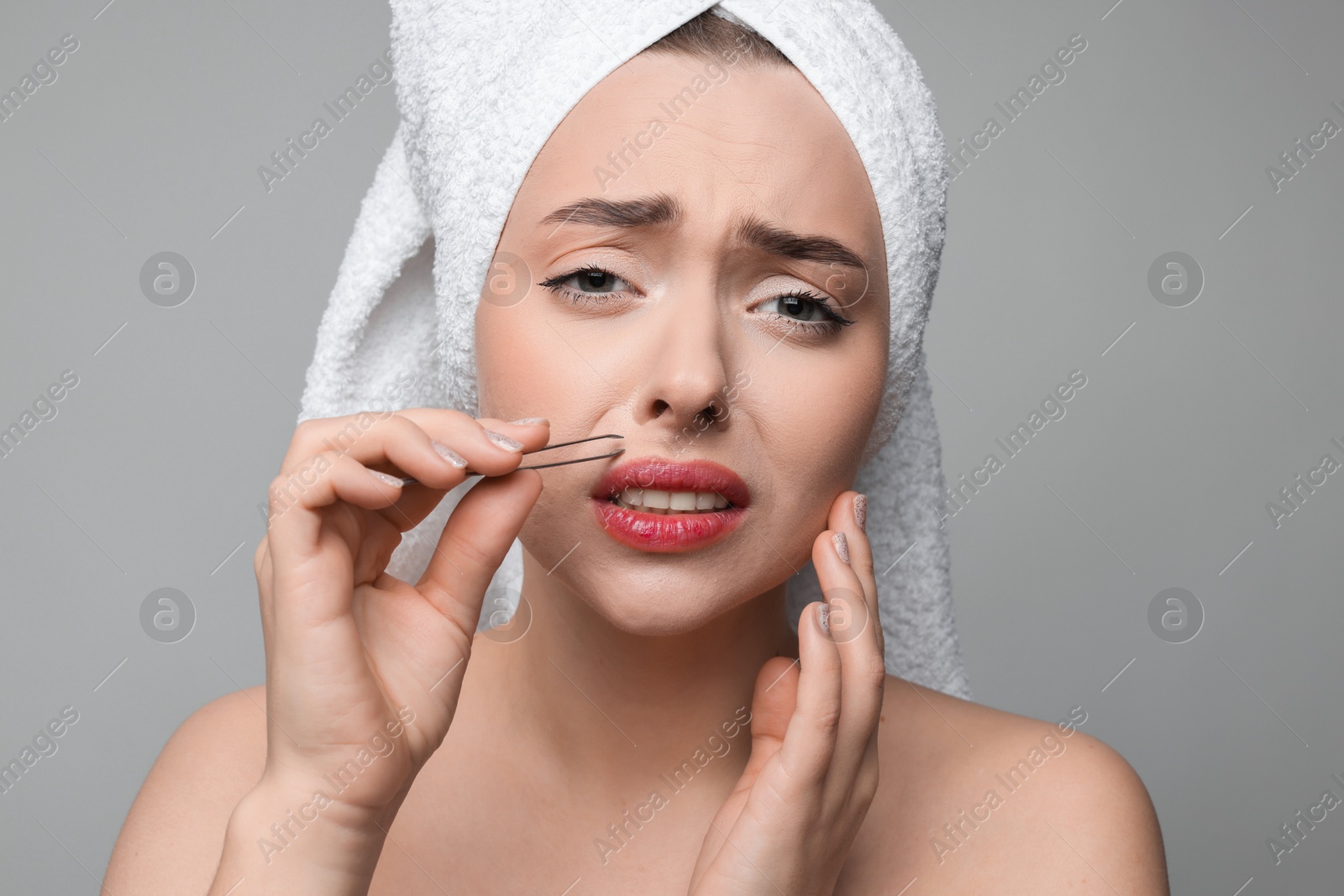 Photo of Beautiful woman plucking her mustache with tweezers on grey background