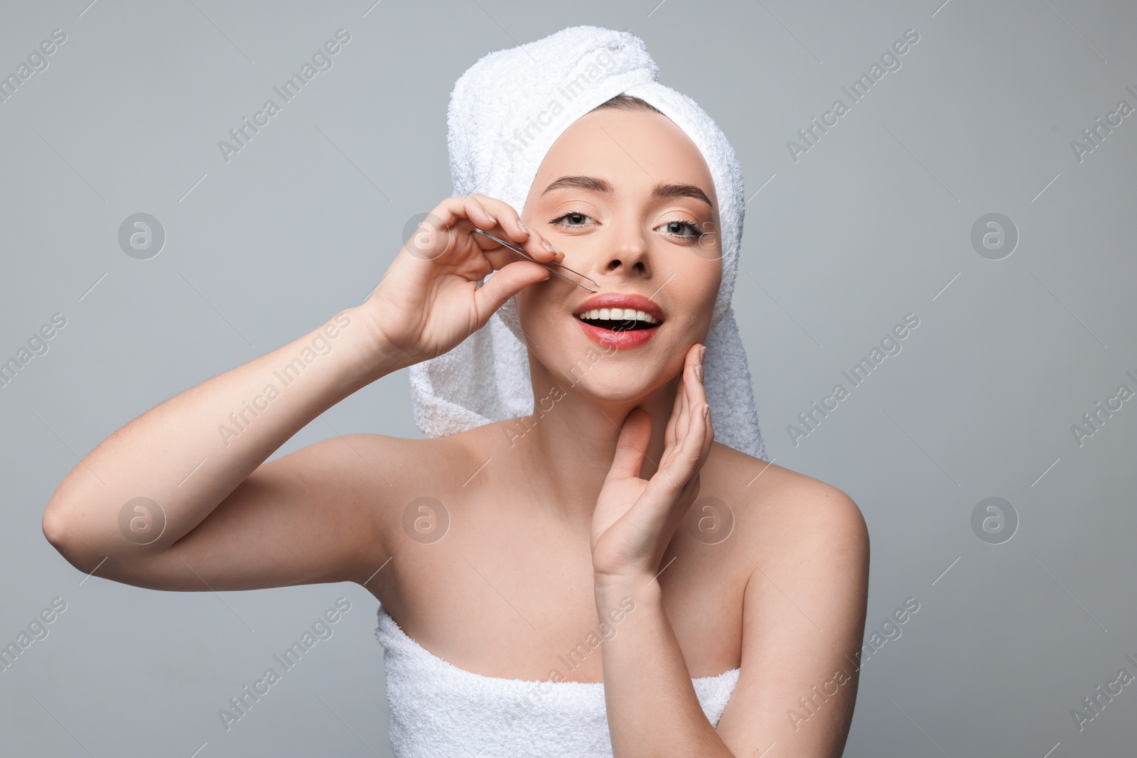 Photo of Happy woman plucking her mustache with tweezers on grey background