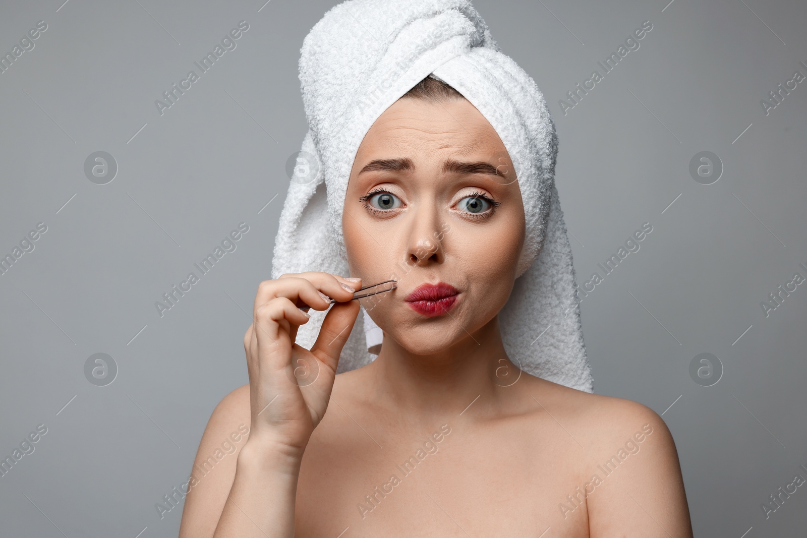 Photo of Beautiful woman plucking her mustache with tweezers on grey background