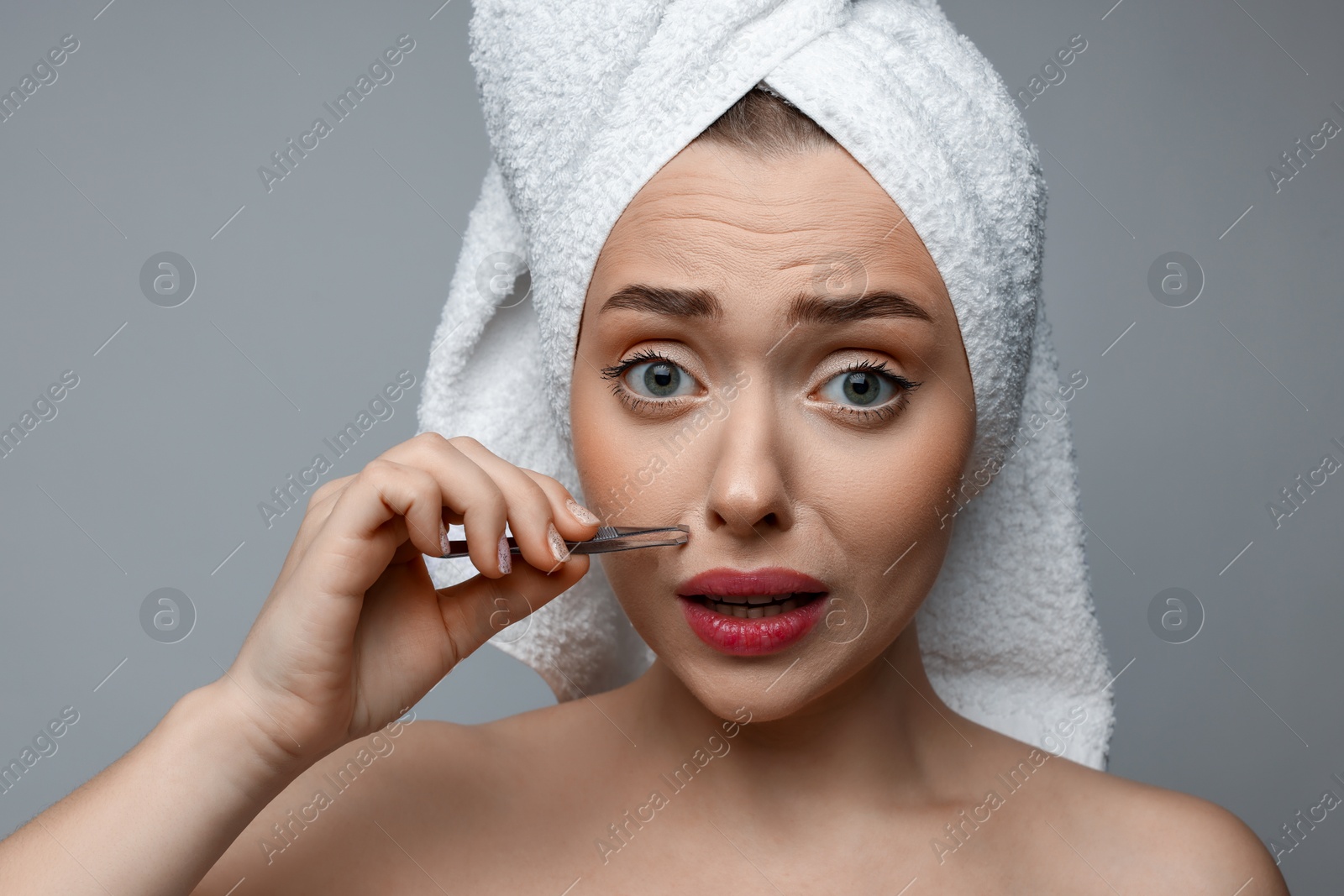 Photo of Beautiful woman plucking her mustache with tweezers on grey background