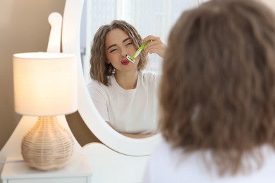 Photo of Beautiful woman shaving her mustache with razor near mirror at home