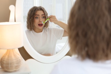 Photo of Emotional woman shaving her mustache with razor near mirror at home