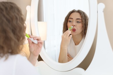 Photo of Beautiful woman shaving her mustache with razor near mirror at home