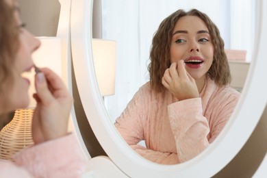 Photo of Happy woman plucking her mustache with tweezers near mirror at home