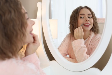 Photo of Happy woman plucking her mustache with tweezers near mirror at home