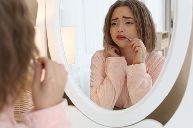 Photo of Beautiful woman plucking her mustache with tweezers near mirror at home