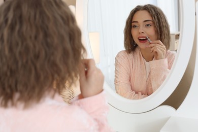 Photo of Happy woman plucking her mustache with tweezers near mirror at home