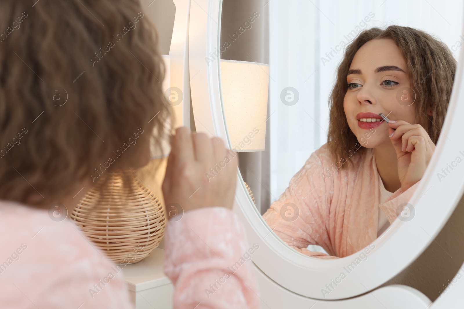 Photo of Happy woman plucking her mustache with tweezers near mirror at home