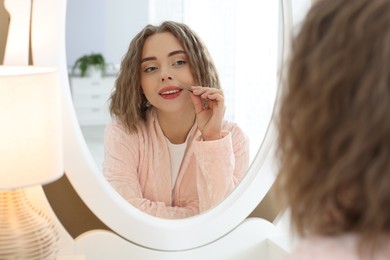 Photo of Happy woman plucking her mustache with tweezers near mirror at home