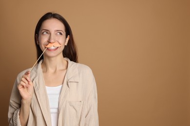 Photo of Happy woman with fake paper mustache on brown background. Space for text