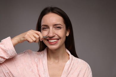 Photo of Happy woman plucking her mustache with tweezers on grey background