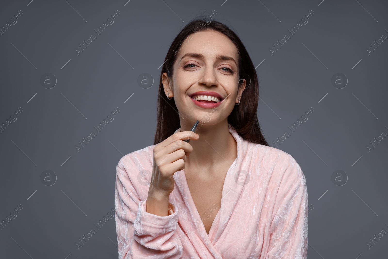 Photo of Happy woman plucking her facial hair with tweezers on grey background