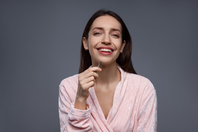 Photo of Happy woman plucking her facial hair with tweezers on grey background