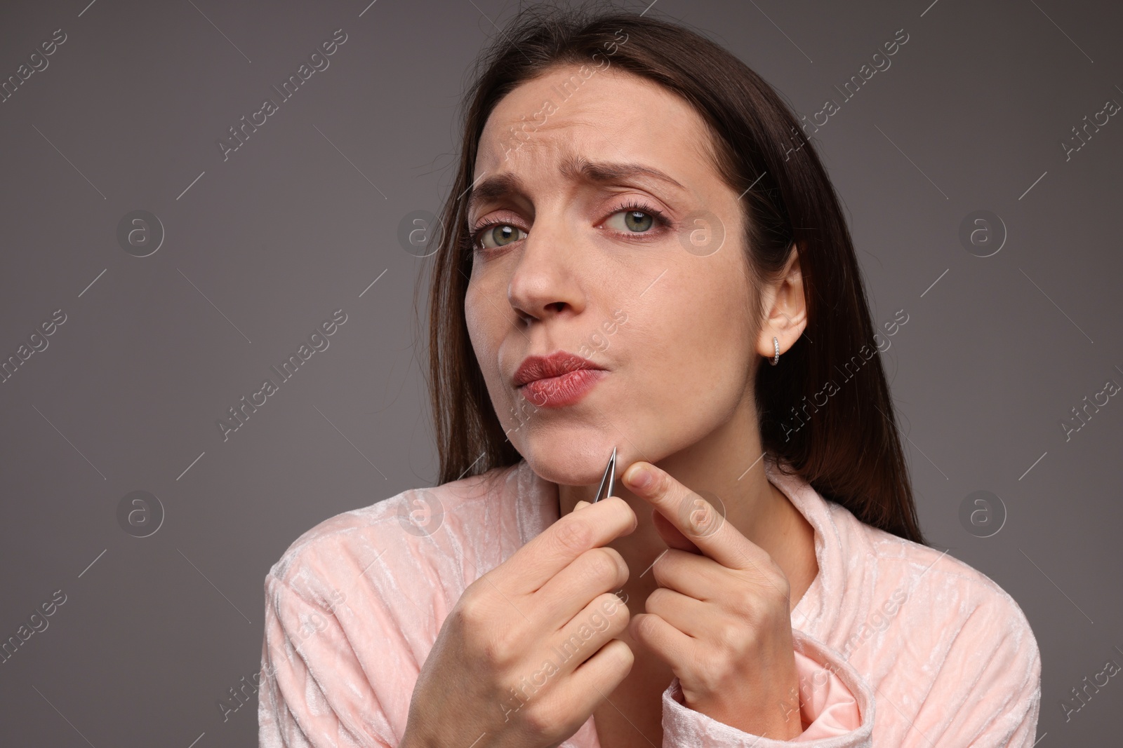 Photo of Beautiful woman plucking her facial hair with tweezers on grey background