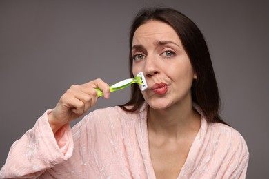 Photo of Beautiful woman shaving her mustache with razor on grey background