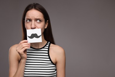 Woman holding paper with drawn mustache on grey background. Space for text