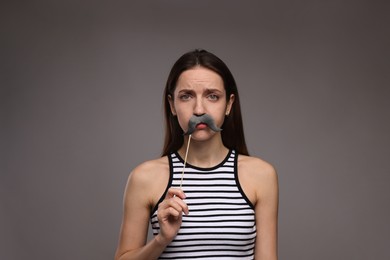 Woman with fake paper mustache on grey background