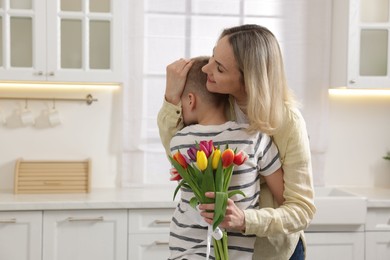 Photo of Happy Mother's Day. Son greeting his mom with flowers in kitchen. Space for text