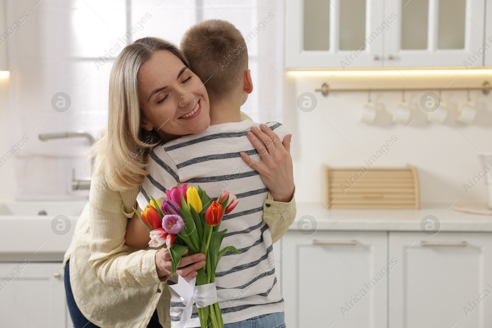 Photo of Happy Mother's Day. Son greeting his mom with flowers in kitchen. Space for text