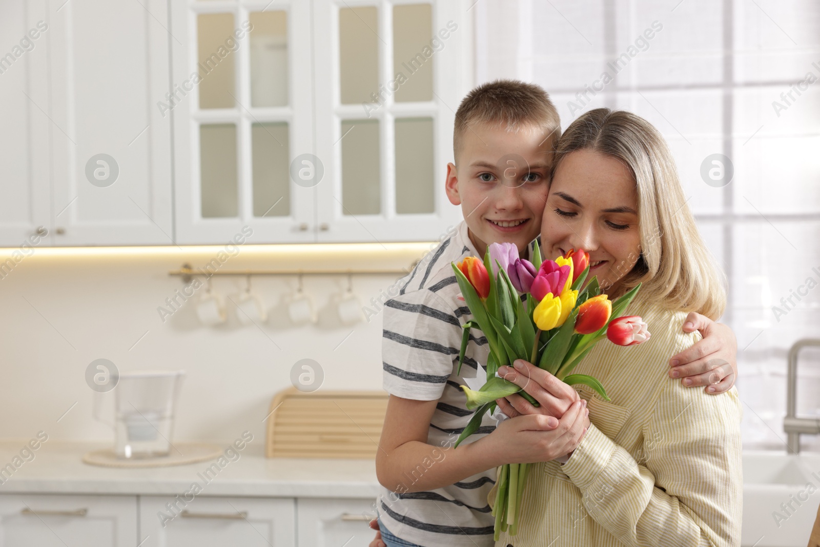 Photo of Happy Mother's Day. Son greeting his mom with flowers in kitchen. Space for text